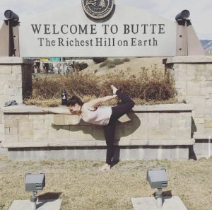 standing bow in from of welcome to Butte sign